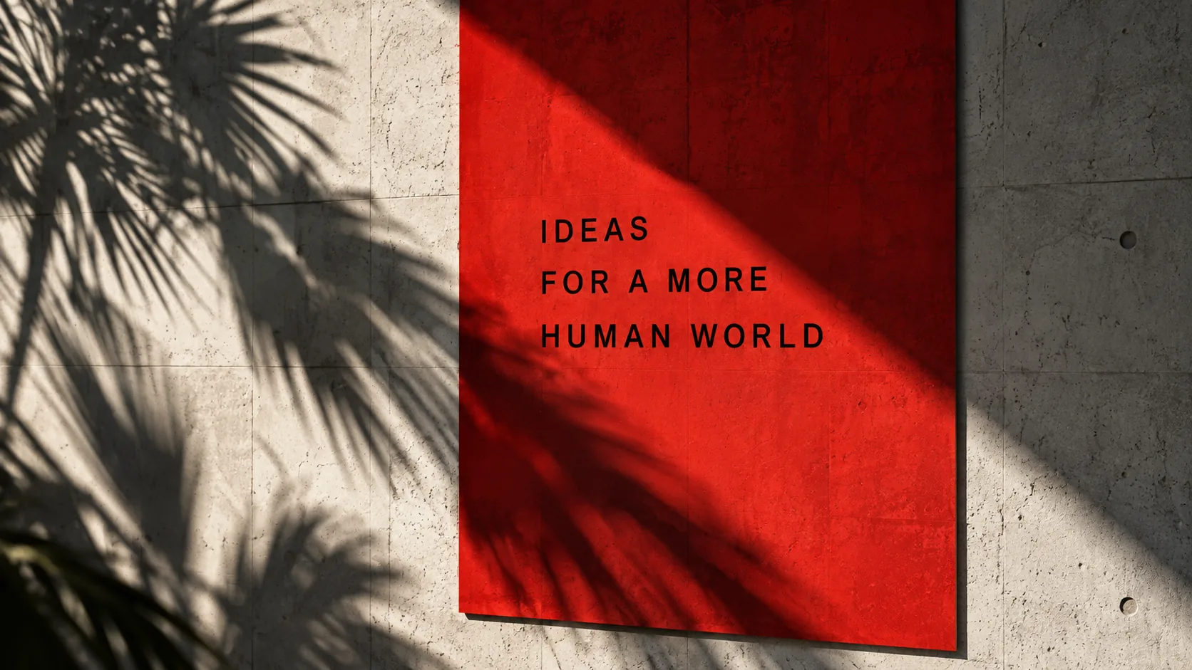 Red panel reading Ideas for a more human world on a concrete wall with palm leaf shadows